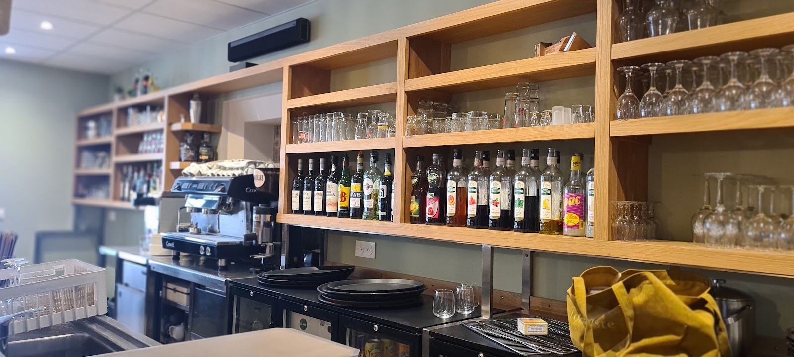 Le bar du restaurant, étagères en bois garnies de bouteilles et de verres, machine à café