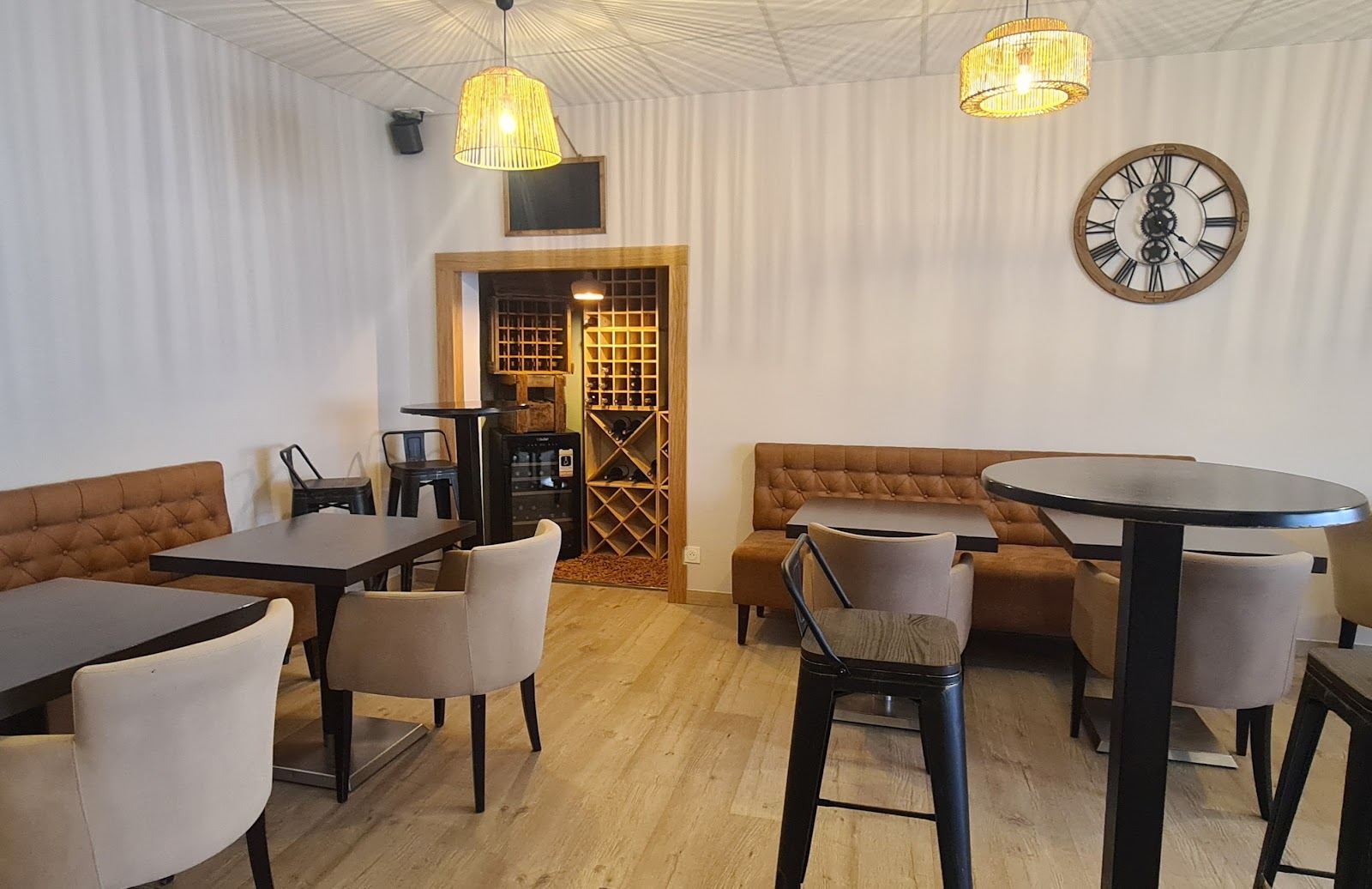 Salle intérieure lumineuse avec banquettes, cave à vin et horloge murale