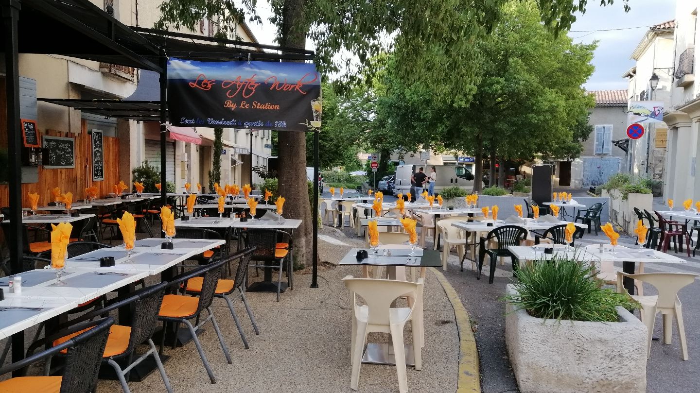 Terrasse du restaurant Le Station avec chaises orange face aux grands arbres