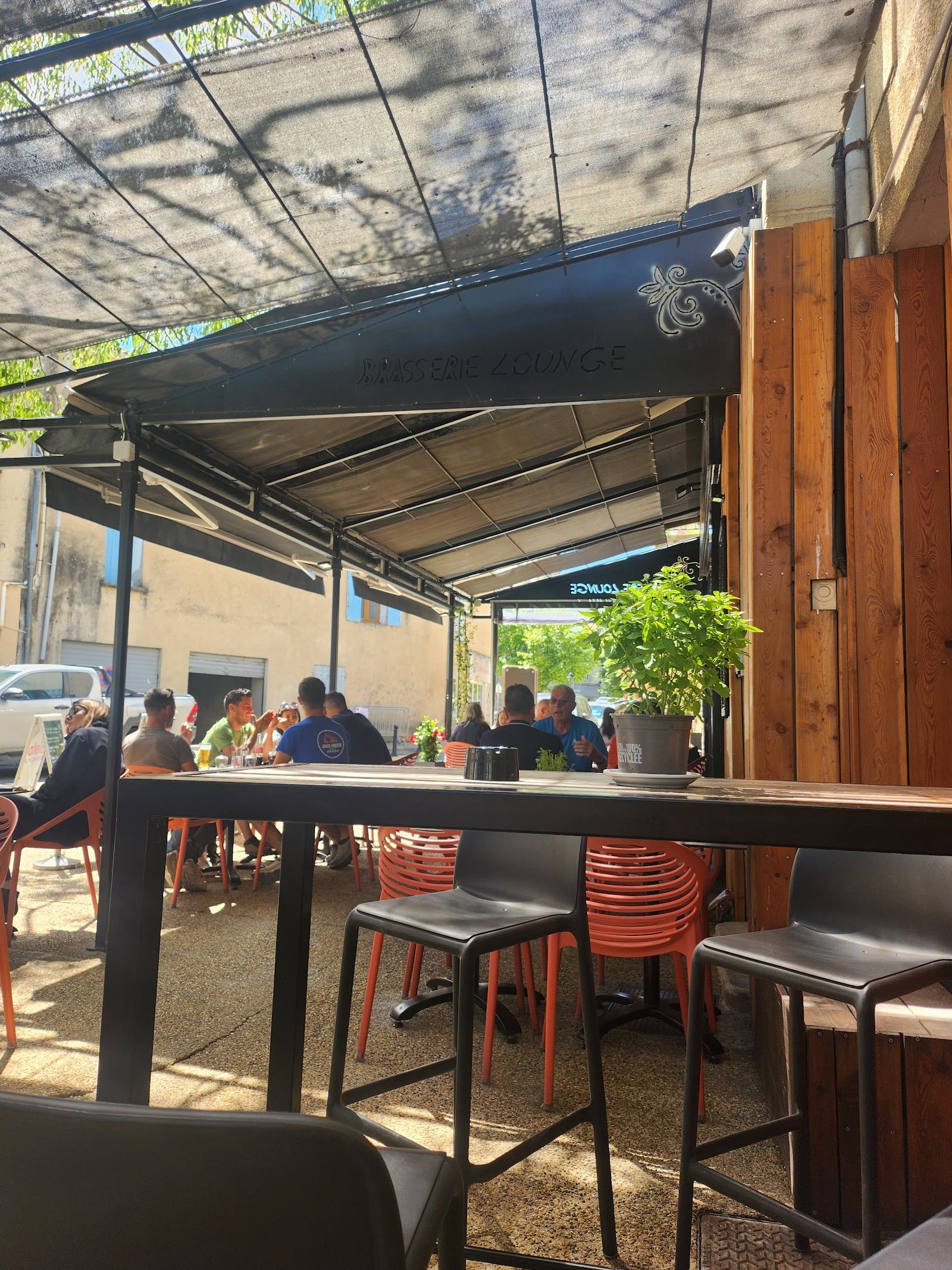 Terrasse du restaurant avec tables en bois, store et chaises orange